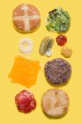 Différents ingrédients d'un hamburger au fromage emballé dans du plastique sur fond jaune — Photo de stock