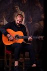 Calvo ragazzo barbuto suonare la chitarra acustica mentre seduto sul palco durante la performance di flamenco — Foto stock