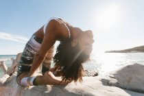 Крупним планом афро-американської привабливою молодою жінкою, що стоїть в міст йоги пози на фоні спокійної води в сонячний день — стокове фото