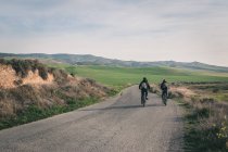 Чоловіки їздять на велосипедах по дорозі в пустельних пагорбах — стокове фото