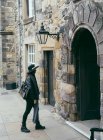 Seitenansicht der trendigen Frau in schwarzem Outfit und Hut zu Fuß auf gepflasterten alten Straße mit Steingebäude, Schottland — Stockfoto