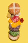 Diferentes ingredientes de um hambúrguer de queijo envolto em plástico sobre fundo amarelo — Fotografia de Stock