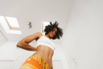 Afro-américain attrayant jeune femme effectuant posture de yoga avec les mains derrière le dos dans la salle de lumière — Photo de stock