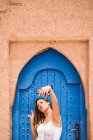 Joyeux jeune femme portant haut blanc avec bikini prenant selfie avec téléphone contre porte orientale bleue en mur de pierre, Maroc — Photo de stock