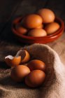 Huevos de pollo y cáscara de huevo con tazón y saco en mesa de madera - foto de stock