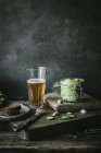 Jar of green cashew pate and glass of beer on wooden board — Stock Photo