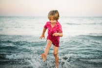 Menino feliz salpicando em águas rasas se divertindo na costa no crepúsculo — Fotografia de Stock