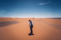 Homme barbu en costume de cow-boy regardant vers le bas tout en se tenant dans le désert contre le ciel bleu — Photo de stock