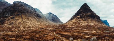 Unrecognizable person wearing red coat walking through picturesque mountains of Scotland — Stock Photo