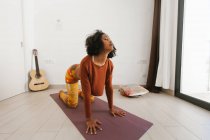 Afro-americano jovem realizando ioga pose com olhos fechados em um tapete em casa — Fotografia de Stock