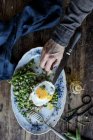 Menschliche Hand Verkostung von serviertem Teller mit sautierten grünen Erbsen und Spiegelei auf Holztisch — Stockfoto