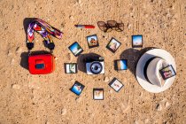 Divers accessoires à la mode et un tas de photos instantanées placées autour de l'appareil photo sur un sol sablonneux le jour ensoleillé de l'été — Photo de stock