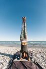 African American young woman in yoga headstand posture on background of calm sea in sunny day — Stock Photo