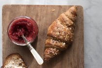 Closeup of crispy croissant with strawberry marmalade served on wooden board — Stock Photo