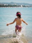 Visão traseira da menina bonito alegre anônimo jogando na água do mar no fundo da costa calma — Fotografia de Stock