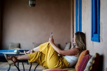 Erwachsene Frau sitzt auf Sofa auf der Terrasse im orientalischen Stil und benutzt Mobiltelefon in Marokko — Stockfoto