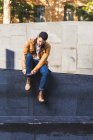 Confident trendy young guy sitting in concrete step outside contemporary building on city street — Stock Photo