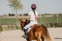 Back view of anonymous girl jockey on horse riding on racetrack on a sunny day — Stock Photo
