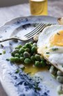 Primo piano del piatto servito con piselli verdi saltati e uovo fritto sul tavolo di legno — Foto stock