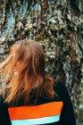 Hermosa mujer joven en sudadera casual ondeando con el pelo de jengibre contra el árbol viejo, Escocia - foto de stock