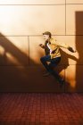Jeune homme positif en tenue élégante sautant près du mur du bâtiment moderne par une journée ensoleillée — Photo de stock