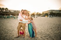 Adult loving man and woman with son and daughters standing together on beach in back lit smiling at camera — Stock Photo