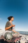 Приваблива молода жінка роздумує і молиться в комірці якамали в позі йоги лотоса на піщаному пляжі в яскравий день — стокове фото
