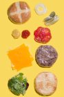 Verschiedene Zutaten eines Käseburgers in Plastik auf gelbem Hintergrund — Stockfoto