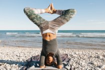 Afrikanisch-amerikanische junge Frau in Yoga-Kopfstand-Haltung vor dem Hintergrund der ruhigen See an sonnigen Tagen — Stockfoto