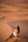 Mujer joven tomando selfie con teléfono en medio del desierto de arena, Marruecos - foto de stock