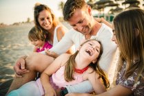 Homme et femme aimant adulte avec fils et filles gais assis ensemble sur la plage dans le dos éclairé — Photo de stock