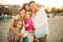 Homme et femme aimants adultes avec fils et filles debout ensemble sur la plage dans le dos éclairé souriant à la caméra — Photo de stock