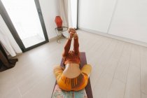 Anonymous woman performing yoga pose and stretching hands on mat in light room — Stock Photo