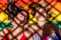 Lésbicas casal deitado na bandeira do arco-íris — Fotografia de Stock