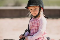 Niña en vestido y heno de jinete sentado a caballo mientras aprende a montar en el hipódromo - foto de stock