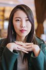 Asian female in stylish green coat looking at camera while sitting at cafe table — Stock Photo