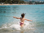 Vista posteriore di anonimo gioioso ragazza carina giocare in acqua di mare su sfondo di spiaggia calma — Foto stock