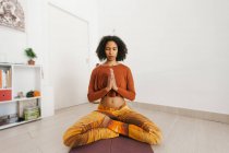 Афроамериканець молода жінка виконує йоги позу з ногами схрещені і розмірковуючи з закритими очима в домашніх умовах — стокове фото