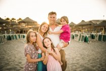 Adulto homem amoroso e mulher com filho e filhas de pé juntos na praia em volta iluminado sorrindo para a câmera — Fotografia de Stock