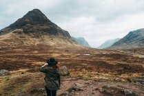 Femme portant et tenant un chapeau debout contre les montagnes pittoresques d'Écosse — Photo de stock