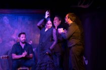 Frau in schwarzem Kostüm tanzt Flamenco neben hispanischen männlichen Musikern während einer Performance gegen Malerei auf dunkler Bühne — Stockfoto