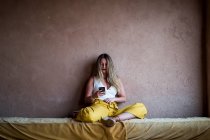 Доросла жінка сидить на дивані на терасі в східному стилі і користується мобільним телефоном у Марокко. — стокове фото