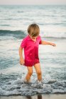 Joyeux petit garçon éclaboussant en eau peu profonde s'amusant sur le bord de la mer au crépuscule — Photo de stock