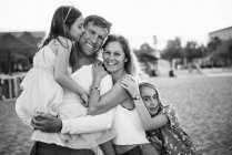 Adult loving man and woman with daughters standing together on beach in back lit smiling at camera, black and white photo — Stock Photo