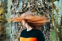 Schöne junge Frau in lässigem Sweatshirt, die mit Ingwer gefärbten Haaren gegen einen alten Baum wedelt, Schottland — Stockfoto