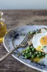 Closeup of served plate with sauteed green peas and fried egg on wooden table — Stock Photo