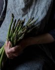 Mulher de colheita em vestido texturizado cinza segurando amontoado ternamente de hastes de espargos verdes frescos — Fotografia de Stock