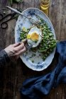 Human hand tasting from served plate with sauteed green peas and fried egg on wooden table — Stock Photo