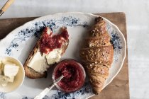 Croissant croccante con pane tostato, burro e marmellata di fragole servito sul piatto su tavola di legno — Foto stock