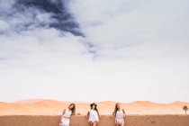 Riga di donne che indossano beachwear bianco in posa alla recinzione di pietra sulla terrazza contro il deserto infinito, Marocco — Foto stock